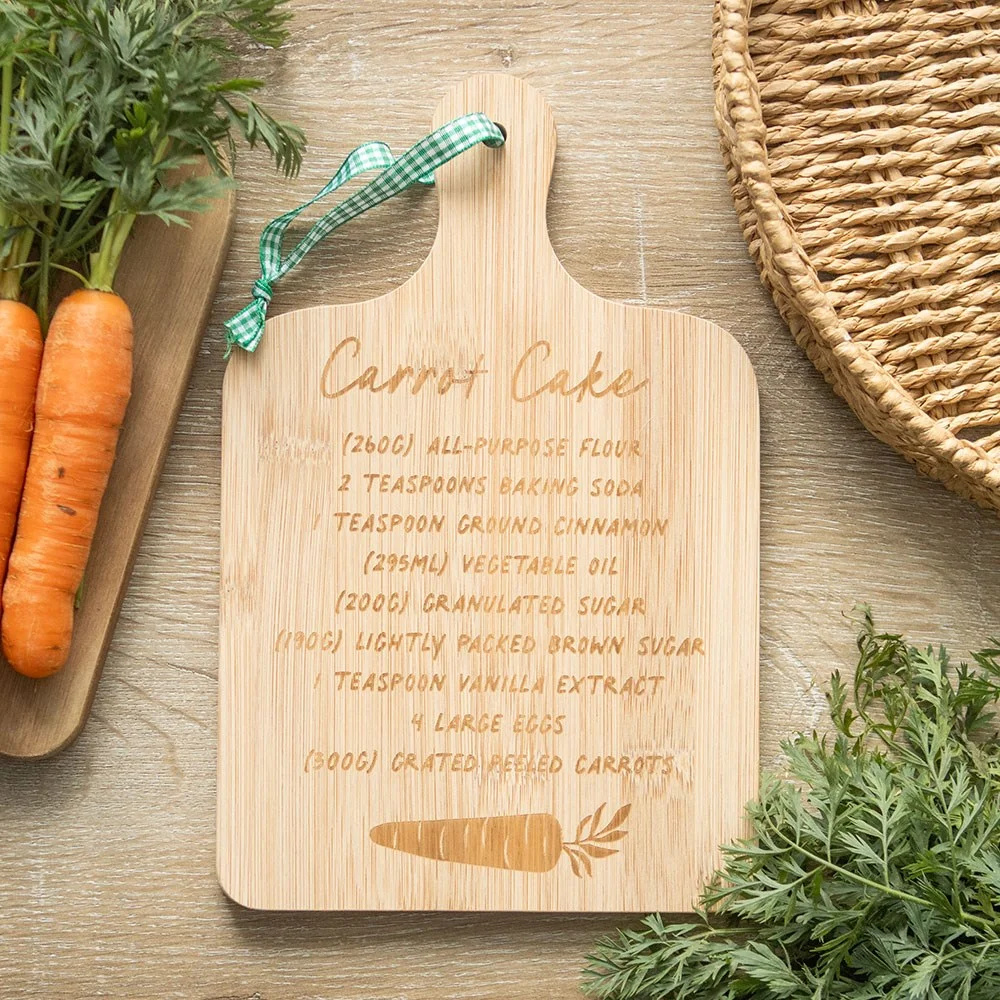Bamboo serving board with a slice of carrot cake and a printed carrot cake recipe card on a wooden surface