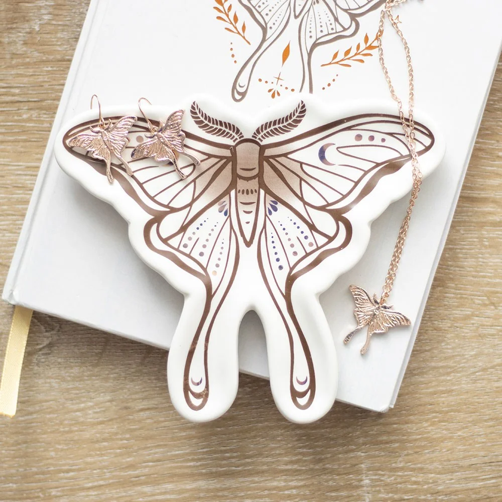 Ceramic luna moth trinket dish with delicate green moth design, holding small jewelry on a wooden surface