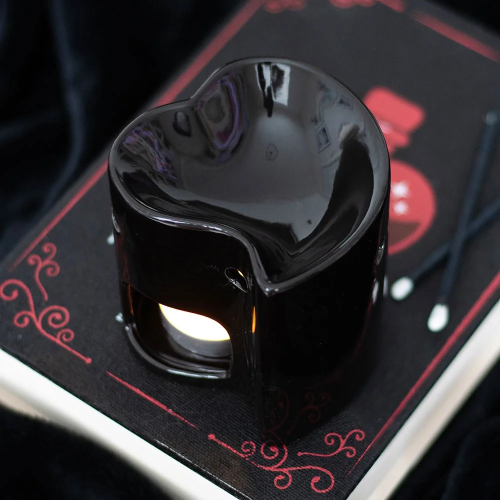 Black ceramic oil burner shaped like a heart with space for tealight and wax warmer on top against white background