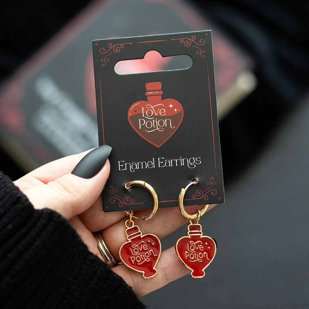 Pair of gold tone earrings with enamel love potion bottle charms on white background
