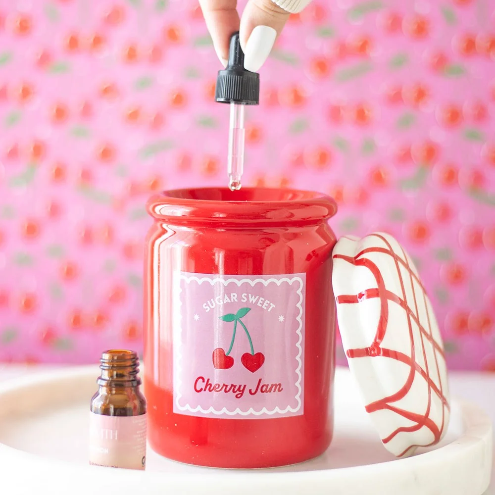 Glossy cherry-red ceramic oil burner shaped like a jam jar with a red and white gingham lid on white background
