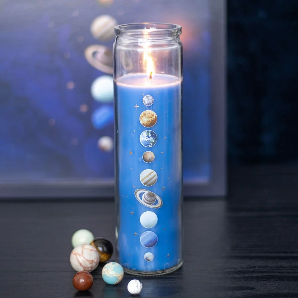 Solar system candle in a glass tube with celestial design and cedar scent, shown lit on a white background