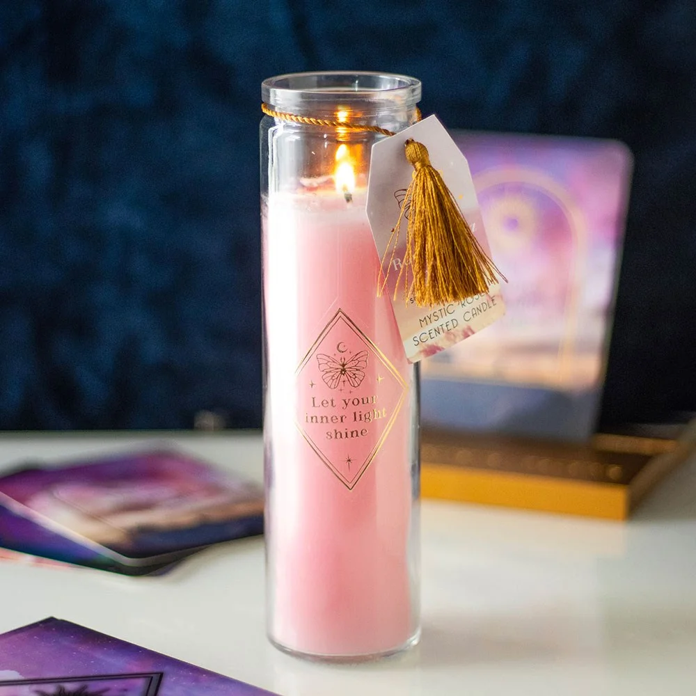 Mystic rose candle in clear tube with gold text and visible rose quartz crystals inside, lit with soft flame glow