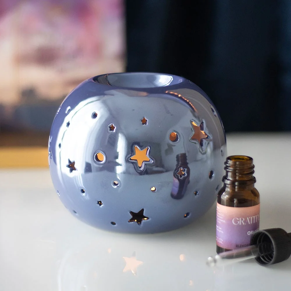 Purple iridescent oil burner with star-shaped cutouts glowing softly against a dark background