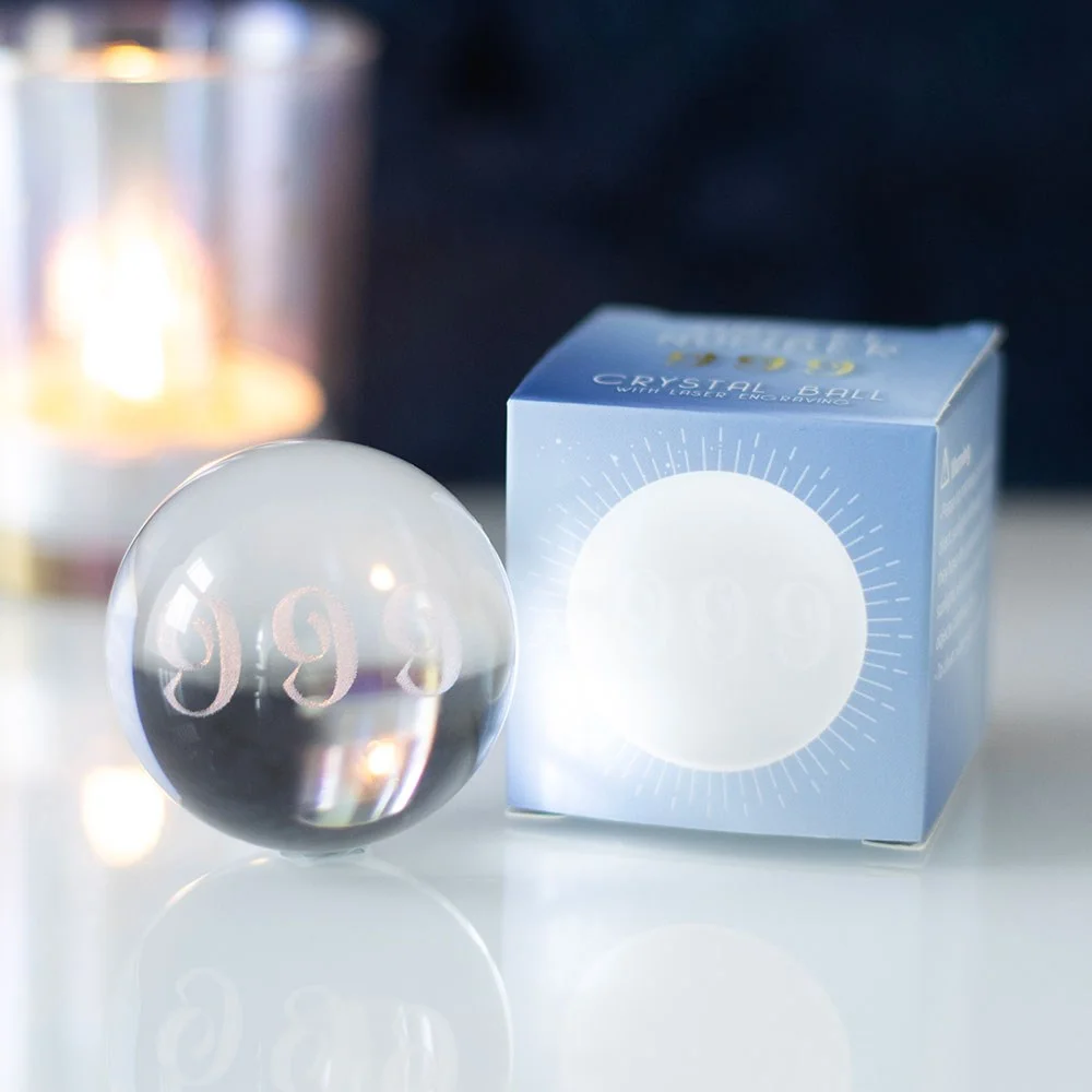 Clear glass angel number crystal ball with laser-engraved 999 inside, resting on a wooden surface