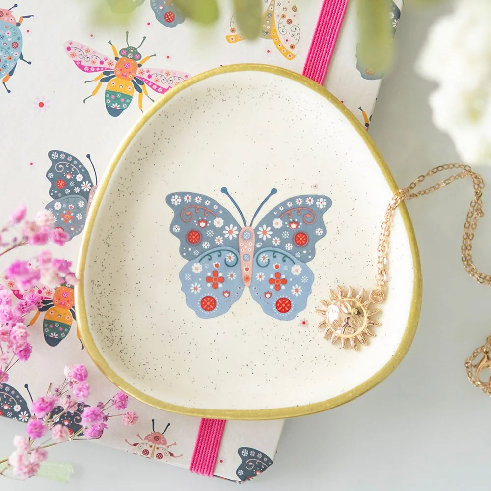 Organic-shaped floral butterfly trinket dish with blue butterfly design, speckled ceramic and gold edging on white background