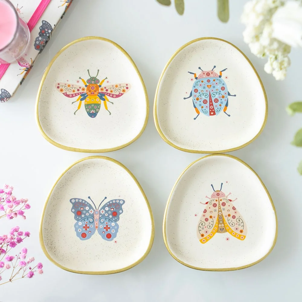 Set of 4 floral trinket dishes with playful bug designs, speckled ceramic finish, and gold edging on a white background