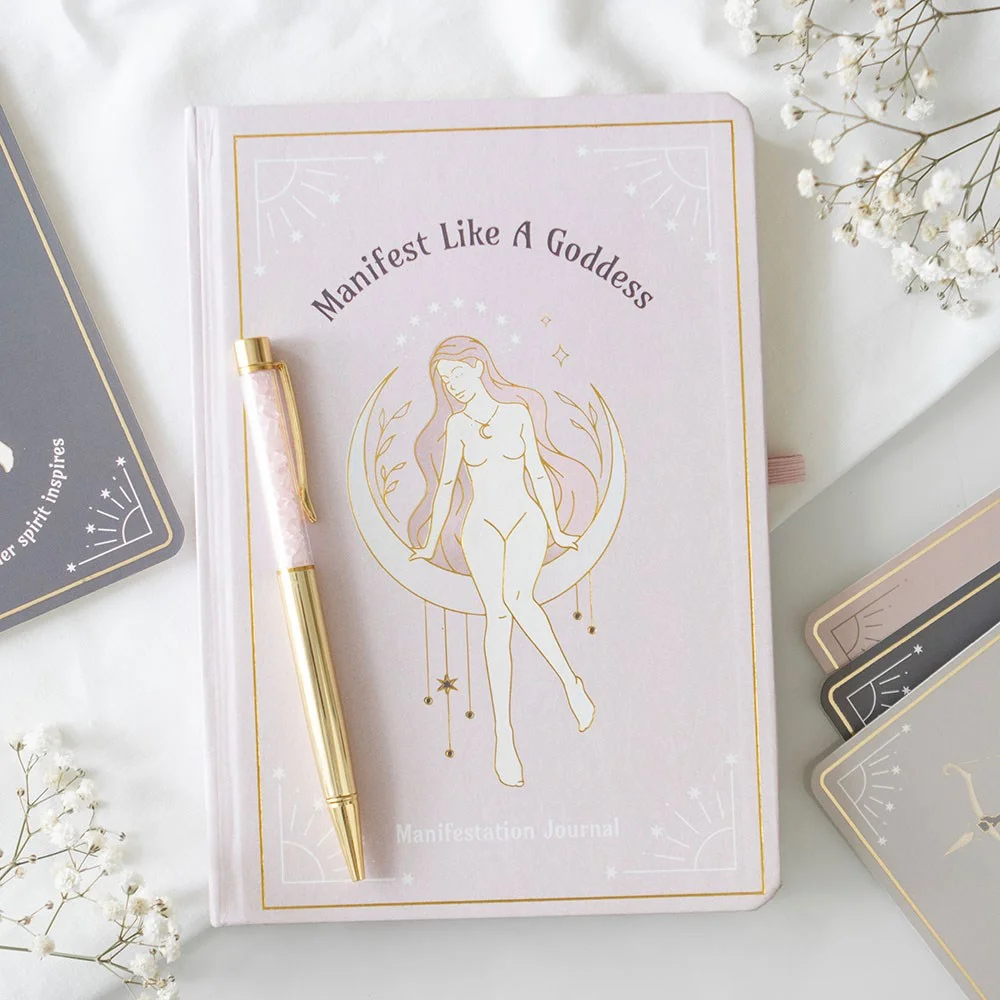 A5 manifestation journal with feminine goddess design and text, paired with a rose quartz crystal chip pen on white background