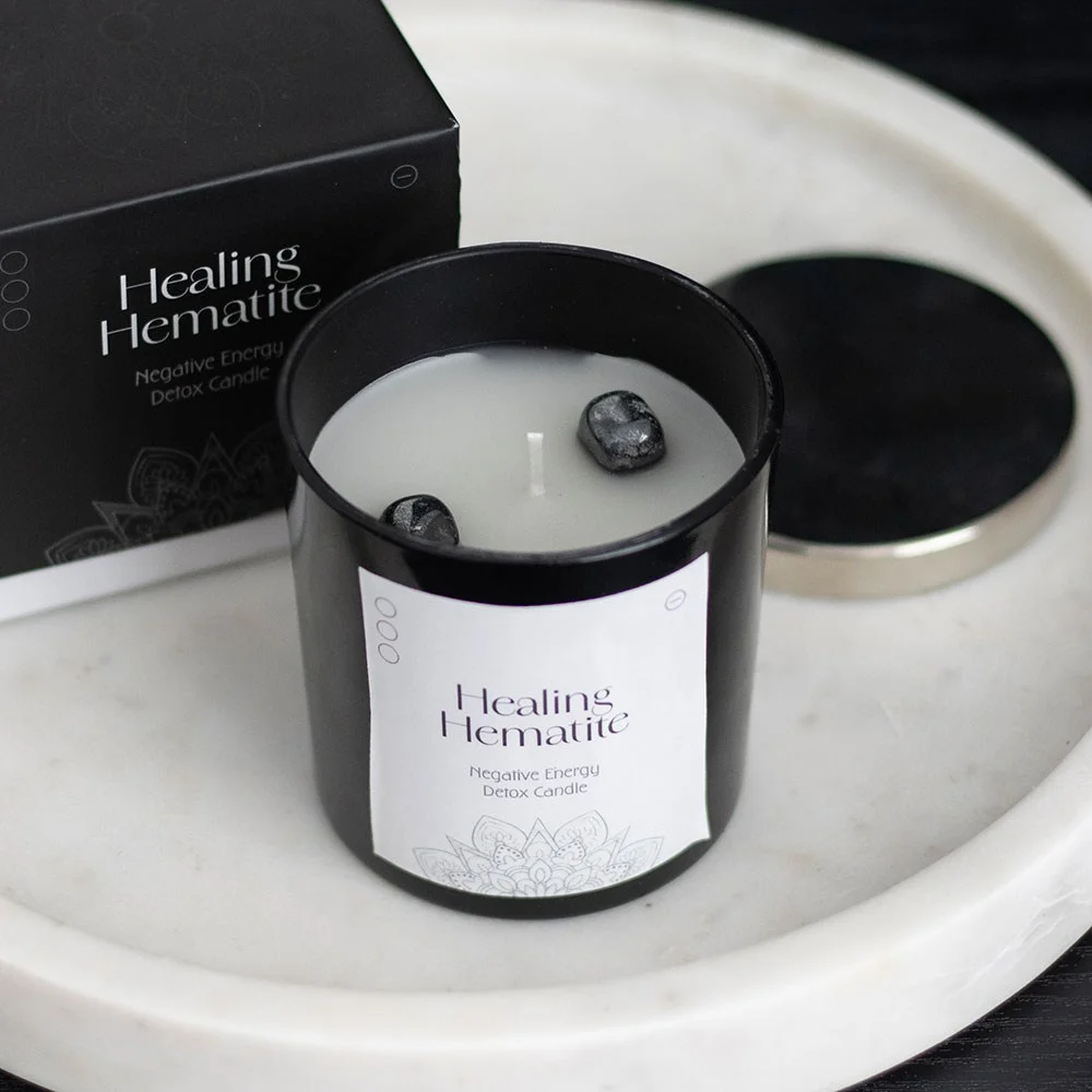 Healing hematite candle in black glass jar with metal lid, polished hematite gemstones inside, on white background