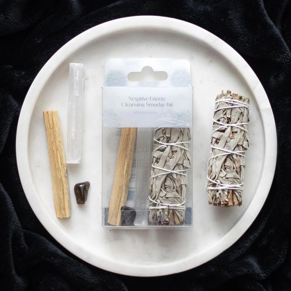 Negative energy smudge kit with white sage bundle, Palo Santo stick, selenite wand, and hematite crystal on white background