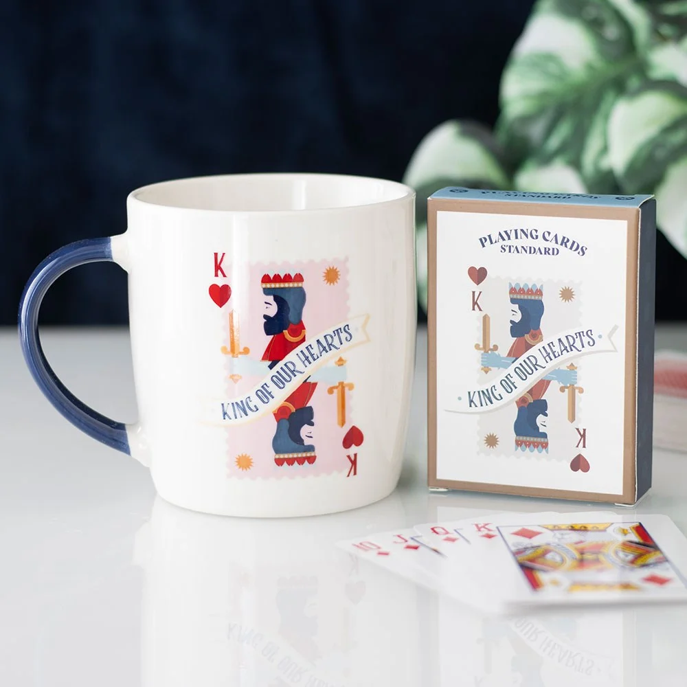 White king of hearts mug with navy handle next to matching deck of playing cards on white background