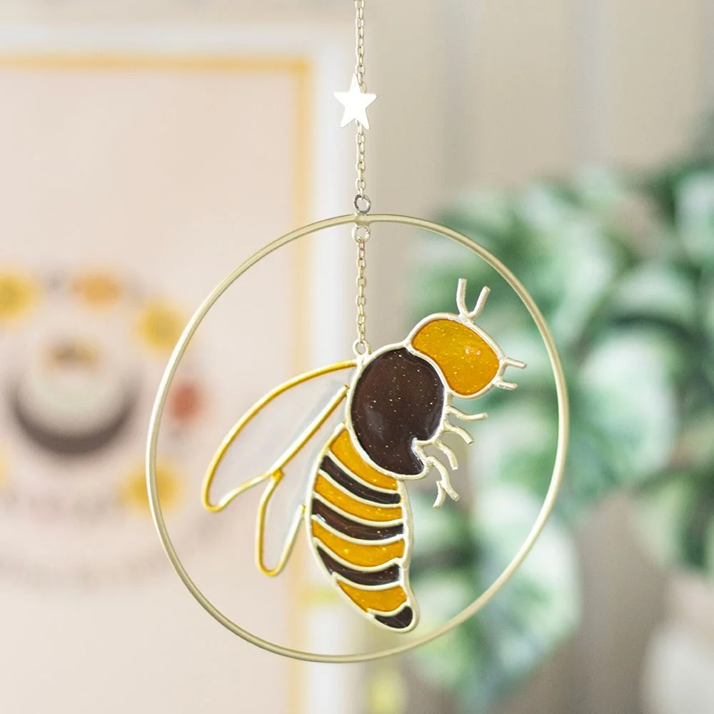 Bee suncatcher featuring detailed bee, star, and crescent moon design in metal and resin hanging in window light