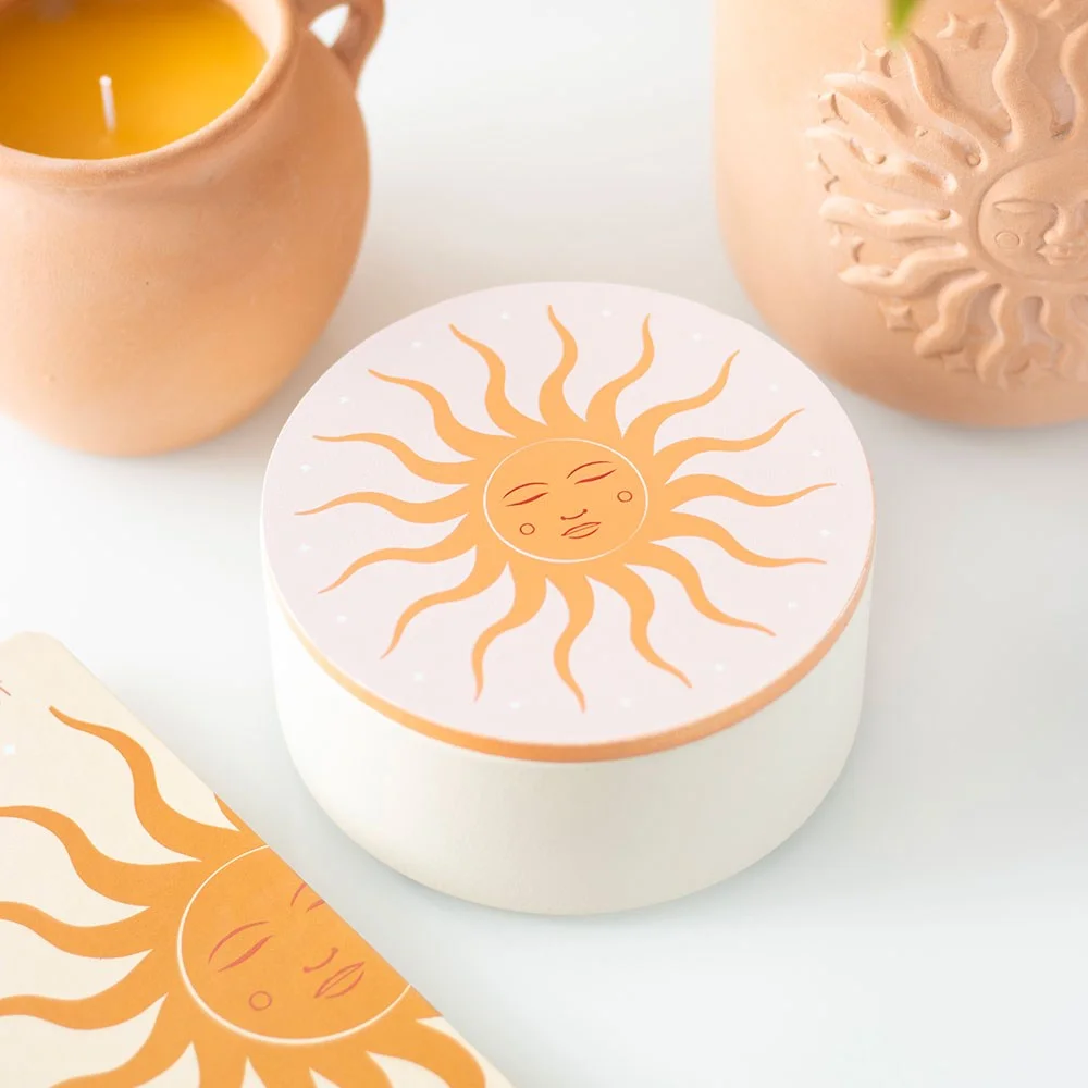 White jewellery storage box with sun design, open to show compartments and mirror on lid, on a bedside table