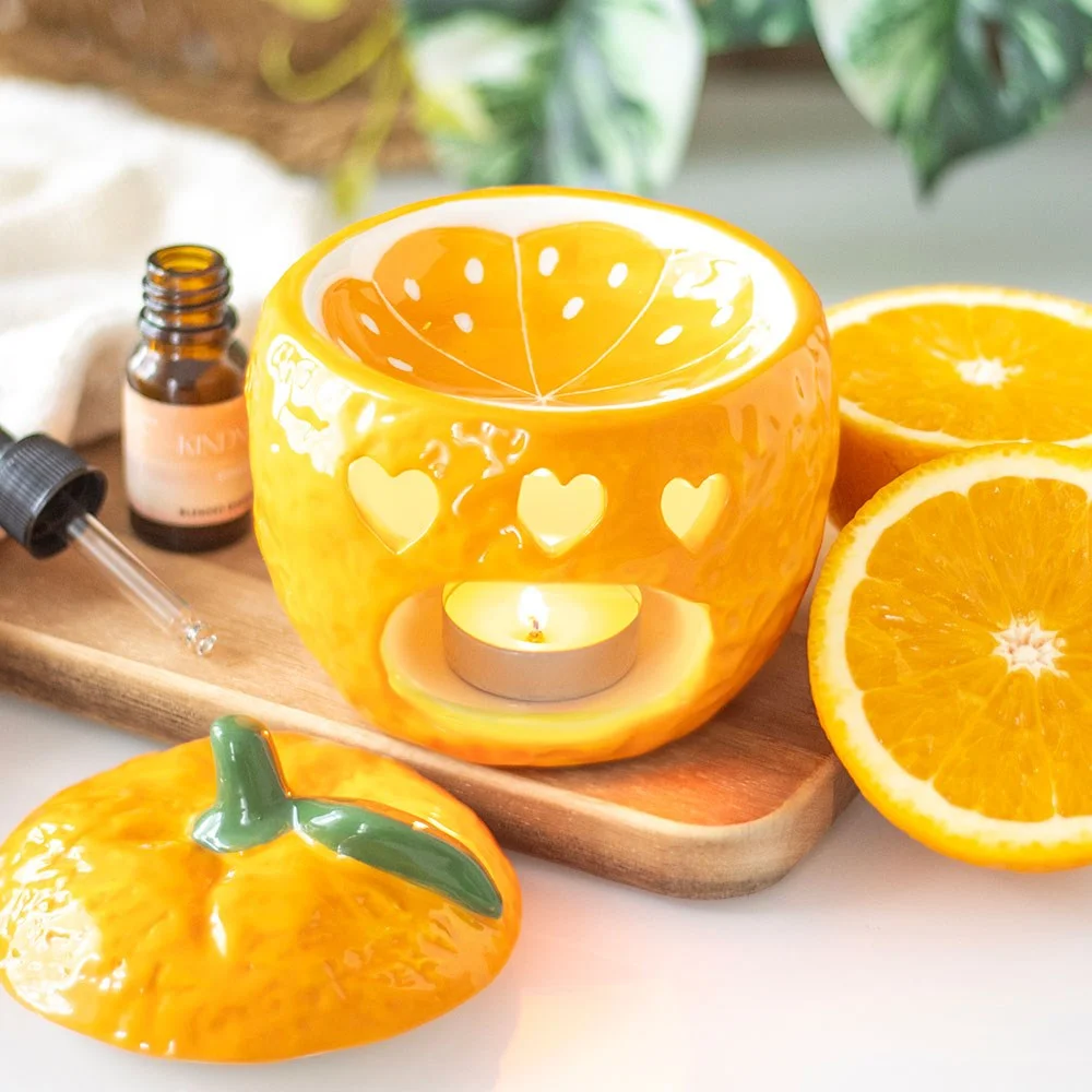 Orange oil burner shaped like a fresh orange with removable lid and dish for fragrance oils, on a white background