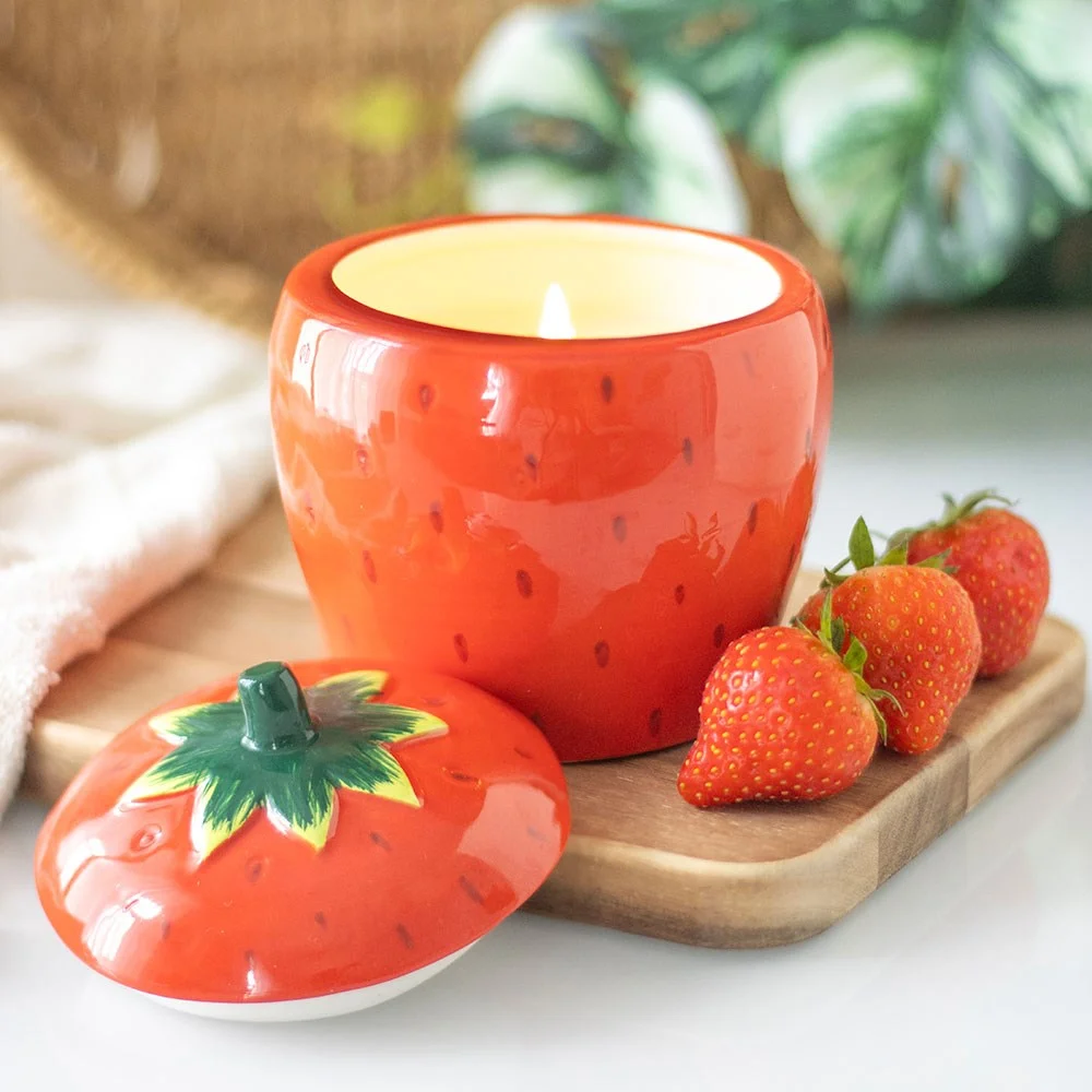 Strawberry candle jar shaped like a fresh strawberry with green leaves, white wax visible inside, on a white background
