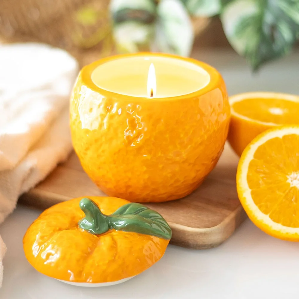 Orange shaped candle jar resembling a fresh orange fruit, designed as a decorative scented candle with a lid on top