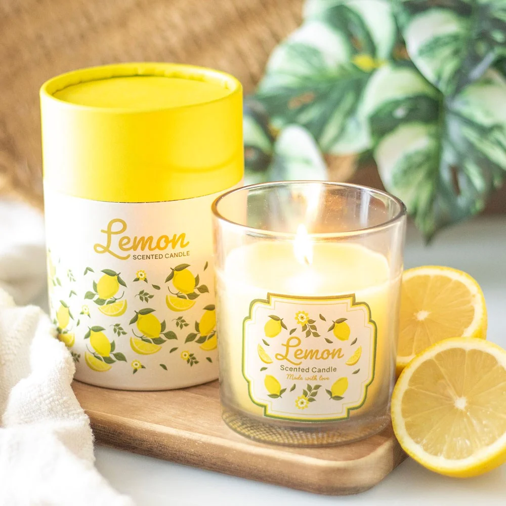 Lemon scented candle in glass holder with lemon print and wooden lid next to matching cylinder gift box