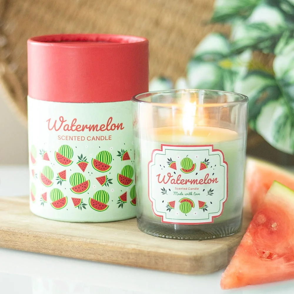 Watermelon scented candle in glass holder with watermelon print and wooden lid next to matching cylinder gift box