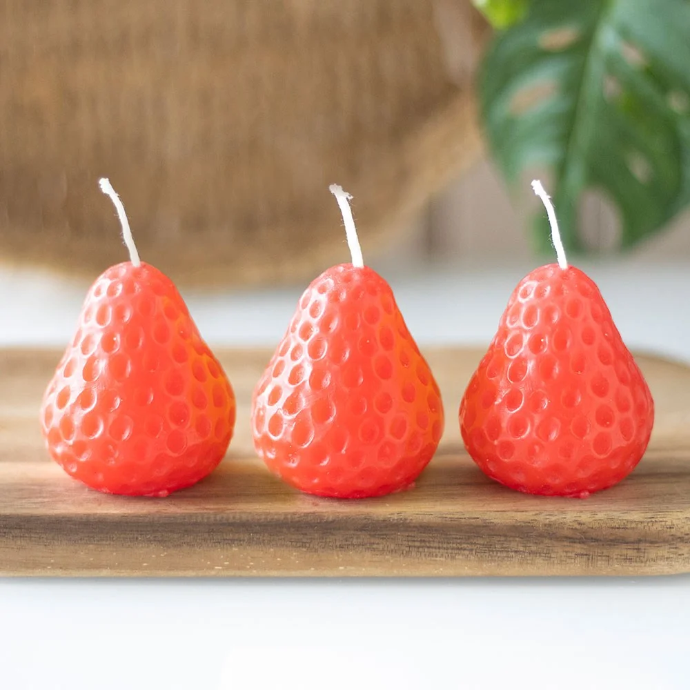 Set of 3 unscented strawberry shaped candles in red with green leaves, arranged on a white background