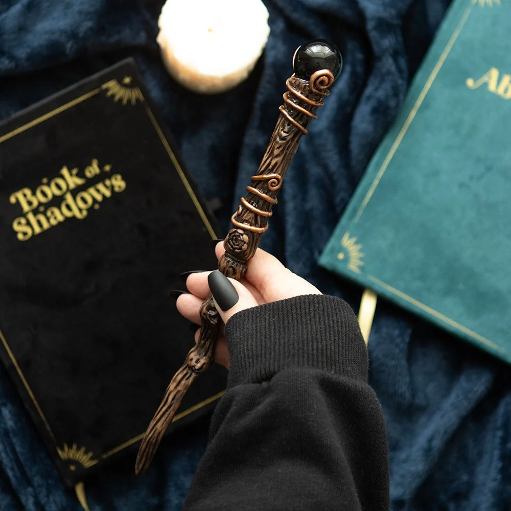 Black obsidian wand with a polished crystal tip and wooden handle, displayed alongside a black storage pouch and gift box