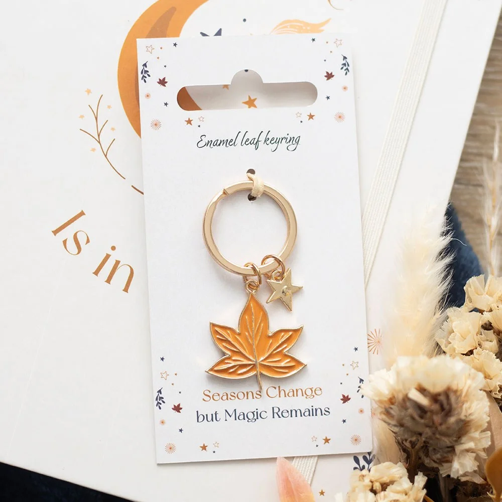 Enamel and metal autumn leaf keyring with warm orange and brown tones on a stainless steel ring against white background