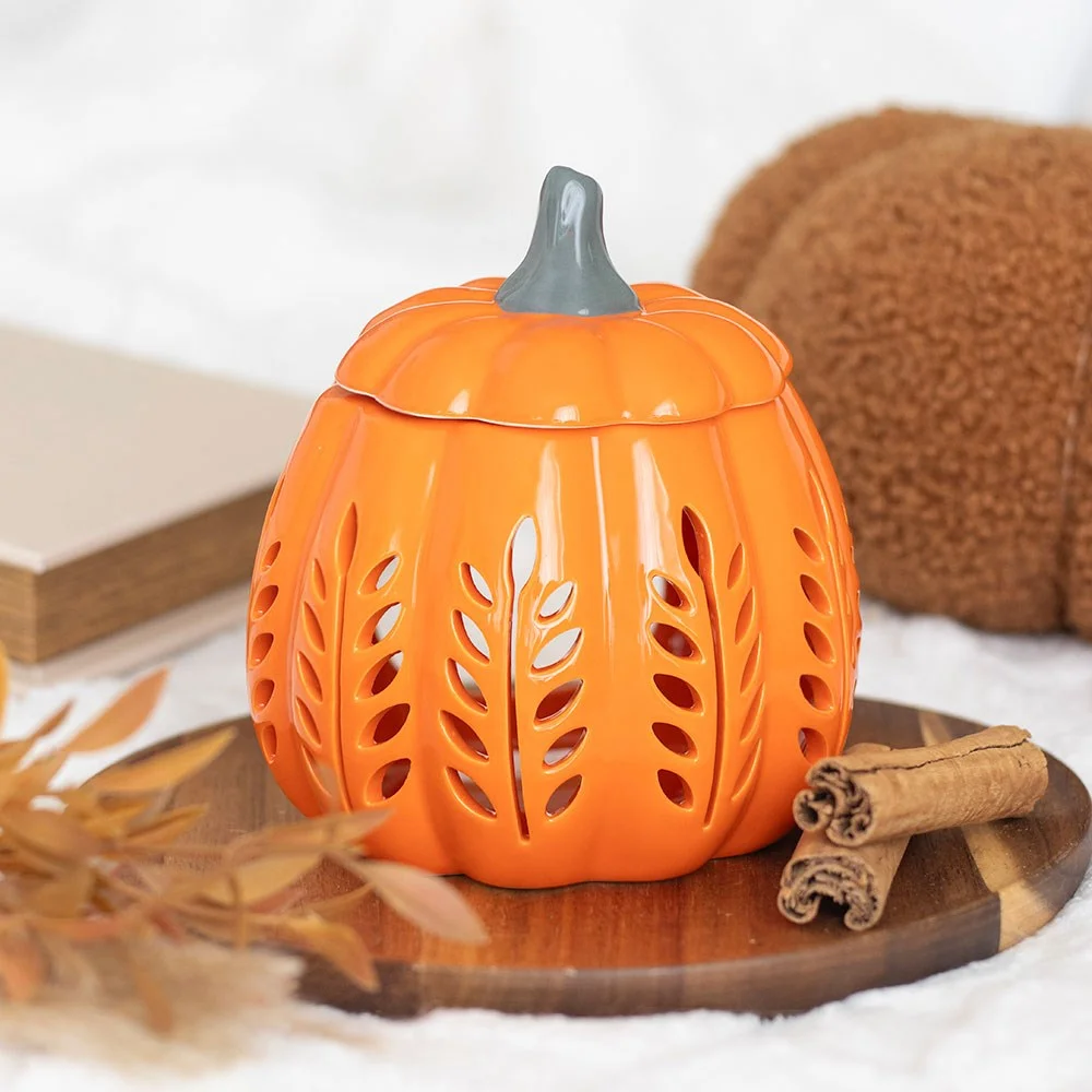 Orange leaf cut out pumpkin oil burner and wax warmer glowing with light inside on a wooden surface