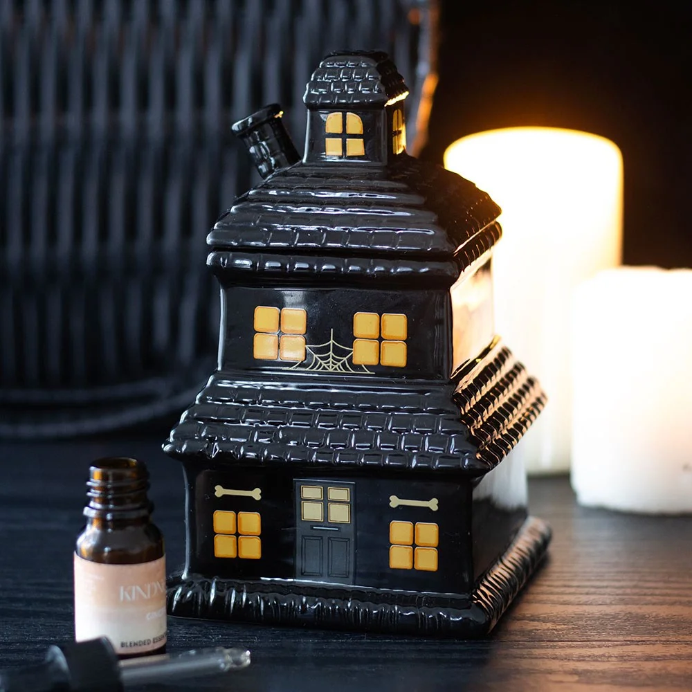 Black haunted house oil burner and wax warmer with lit tealight glowing inside, designed for wax melts and oils