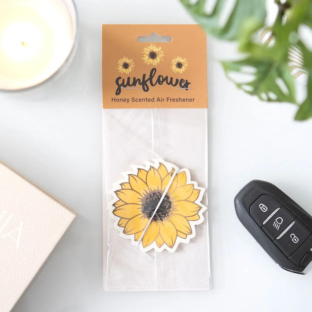Sunflower-shaped air freshener with honey scent, bright yellow petals and green leaf detail hanging in car interior
