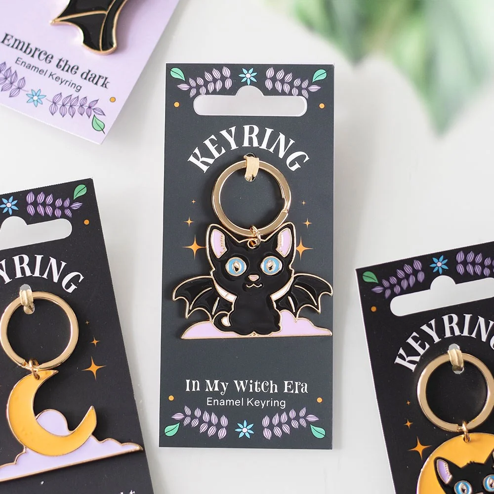 Black cat with bat wings enamel witch era keyring on backing card, gothic magical accessory for keys or bags