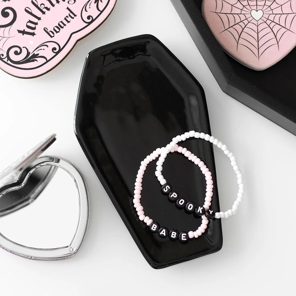 Black coffin trinket tray made of black ceramic, shaped like a coffin, holding small jewellery and keys on a table