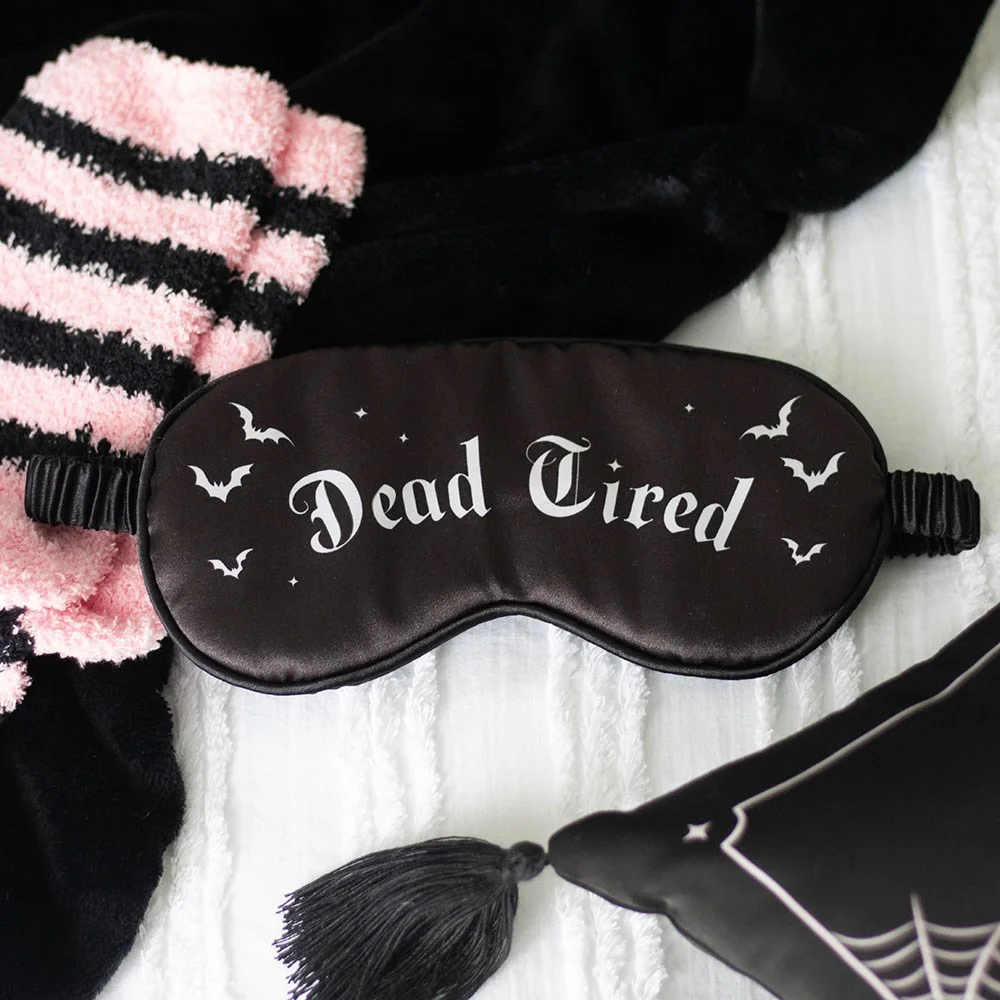 Black satin sleep mask with "Dead Tired" embroidered in gothic font, designed to block out light for better sleep