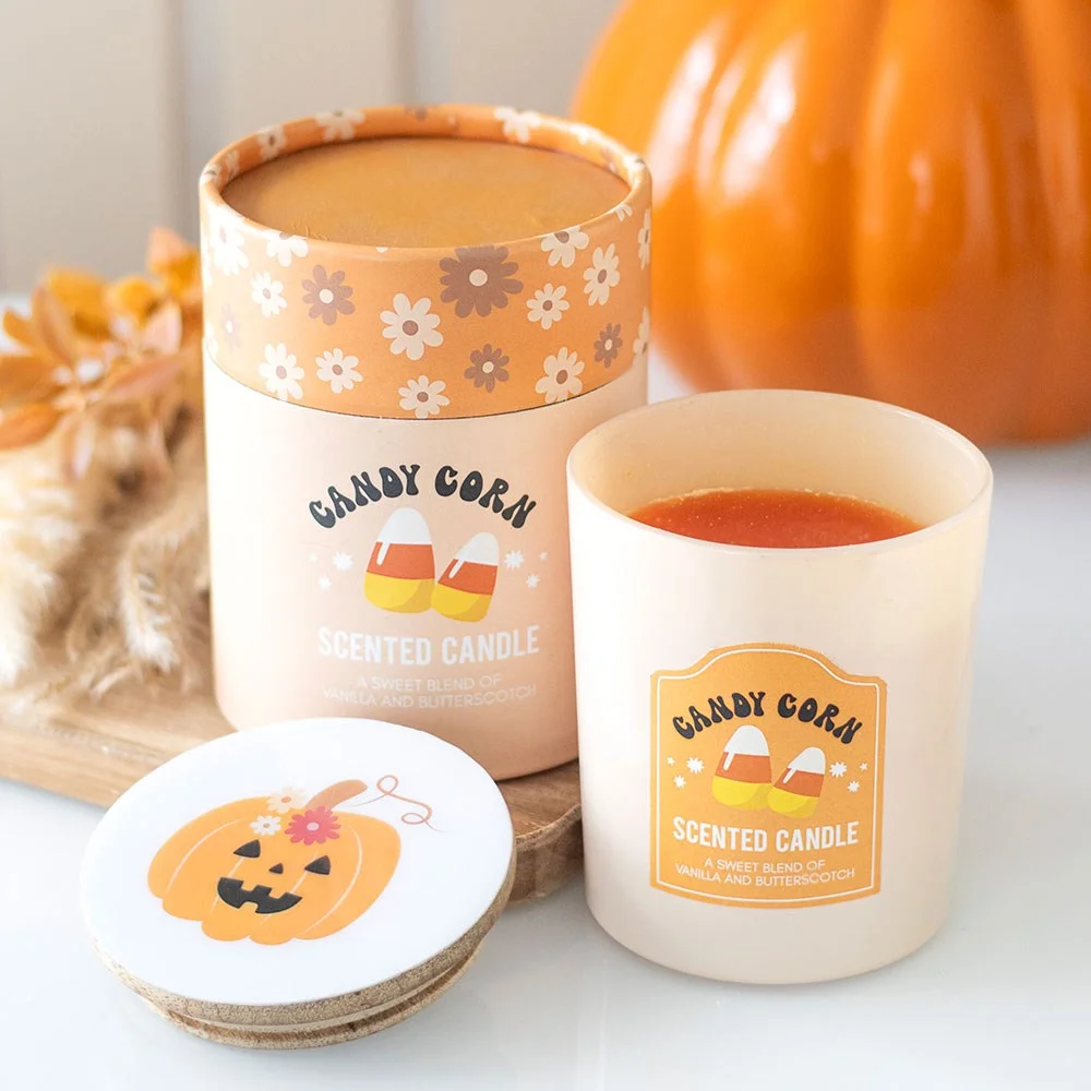 Candy corn candle in glass holder with wooden lid featuring pumpkin and candy corn designs next to matching gift box