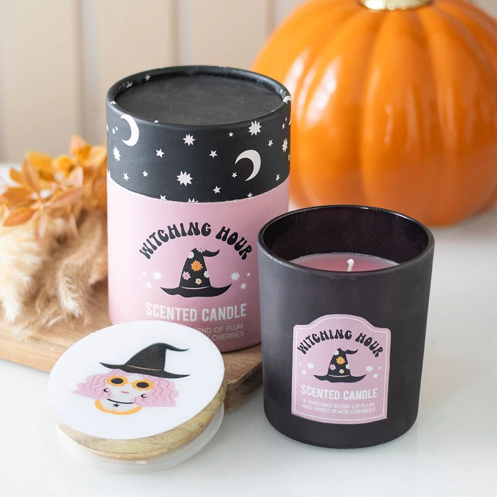 Witching hour candle in glass holder with wooden lid featuring witch designs, next to matching cylinder gift box