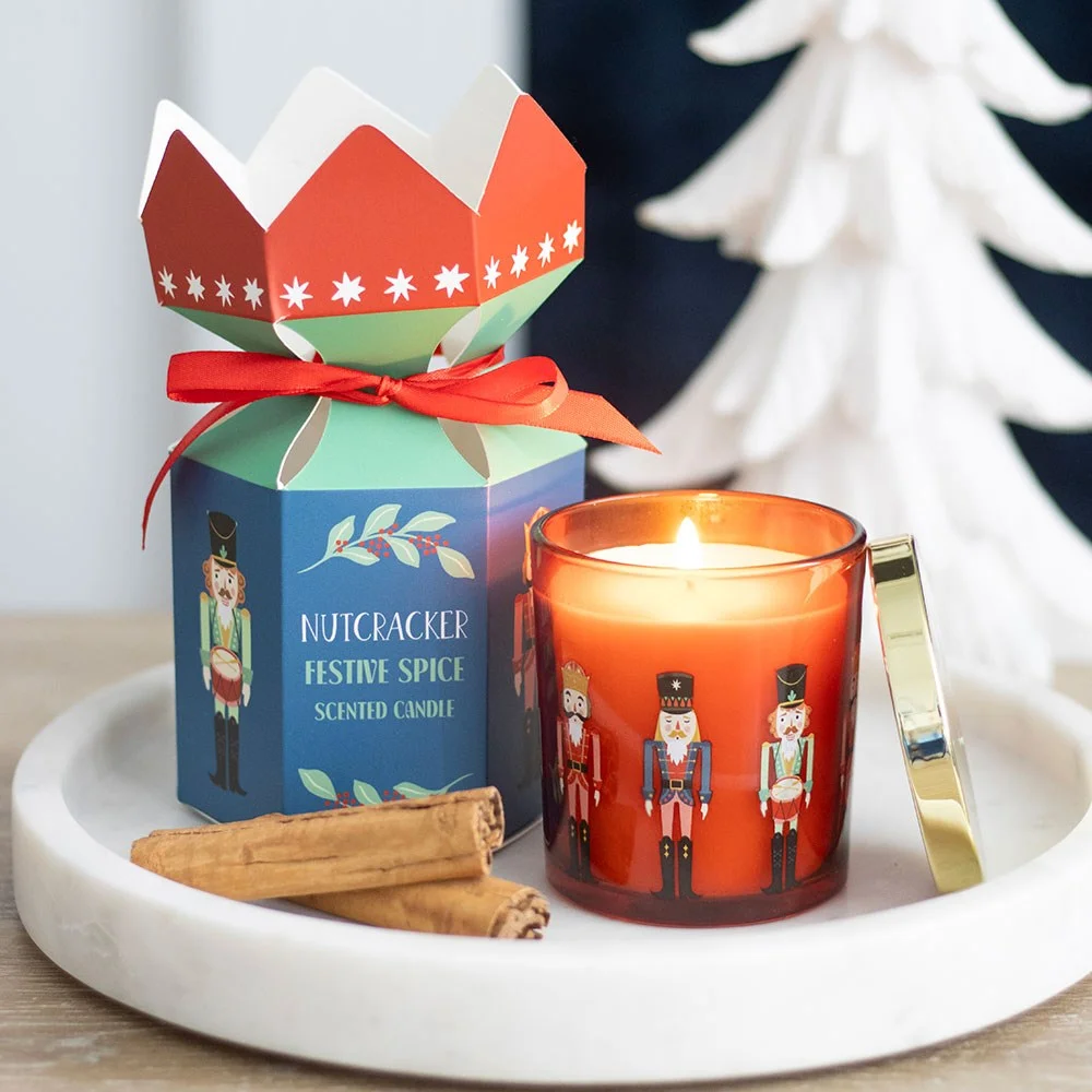 Nutcracker scented candle with gold-tone lid, festive spice fragrance, presented in matching cardboard box, 25‑hour burn.