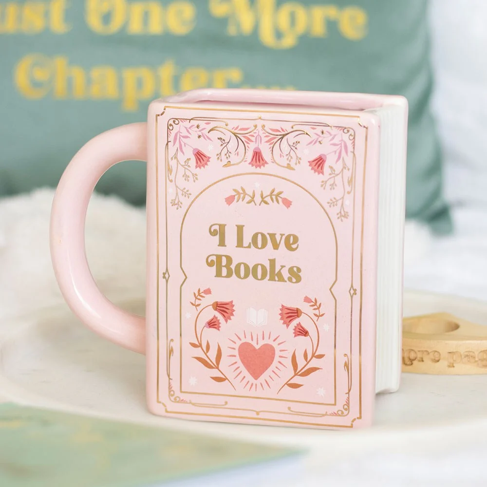 Pink ceramic book shaped mug with “I Love Books” inscription holding a cup of coffee