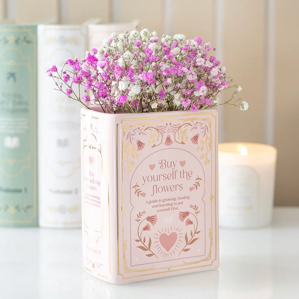 Pink book vase, ceramic vase shaped like an upright book, on a desk or bookshelf, holds fresh or dried flowers