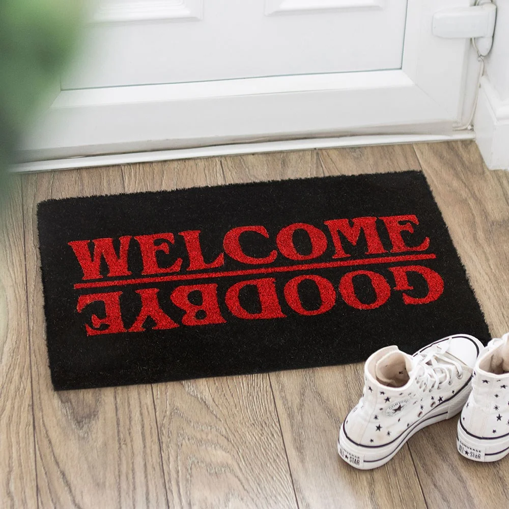 Bold black welcome doormat with bright red 'Welcome' and upside‑down 'Goodbye' on coir surface.