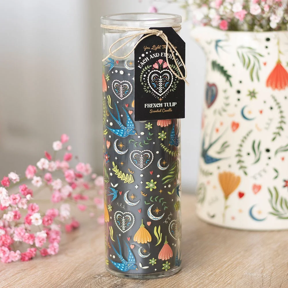 Tall glass French tulip candle in a black Midnight Bloom print tube with lit wick on a white background