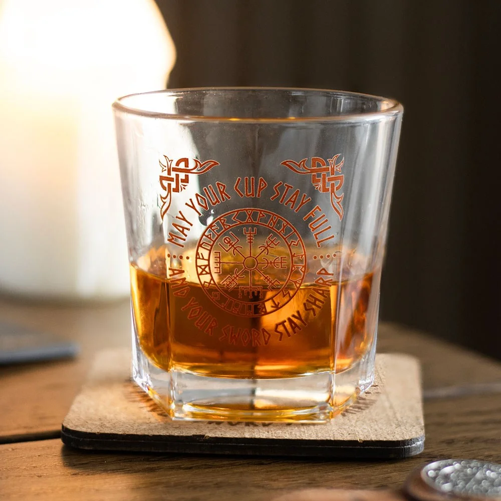 Viking compass glass filled with whiskey next to matching cork coaster with Vegvisir symbol on white background
