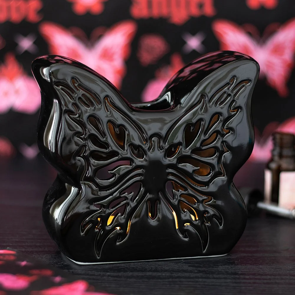 Black butterfly oil burner with intricate cut-out design, lit tealight inside casting warm glow through butterfly shapes