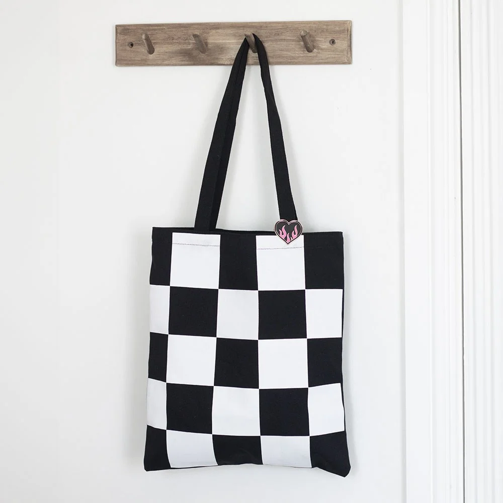 Black and white checkerboard tote bag with detachable enamel heart pin badge on front pocket