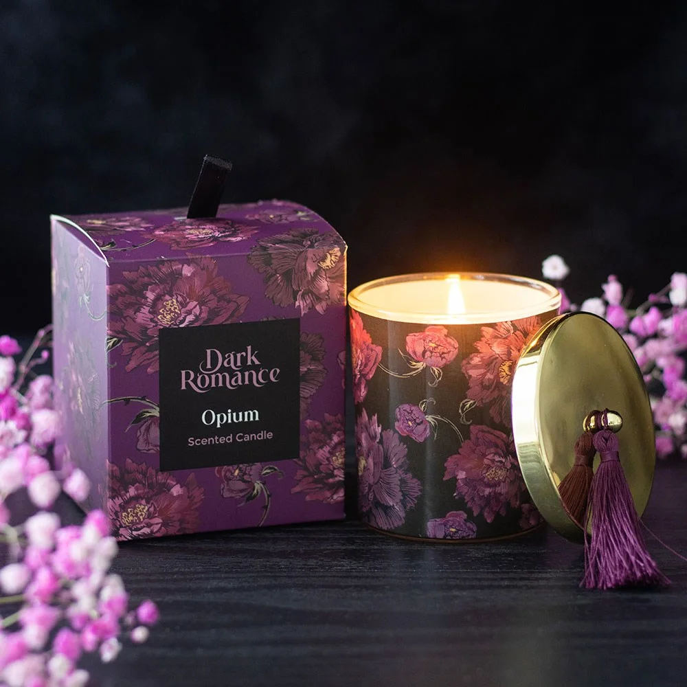 Opium scented candle in a lidded glass holder wrapped with purple blooms and topped with a tassel on a white background