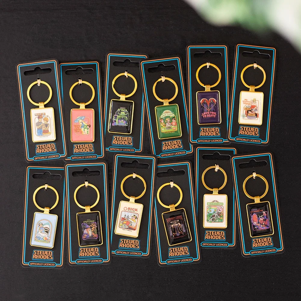 Display of 48 Steven Rhodes enamel keyrings set featuring dark humor and retro designs on a countertop stand