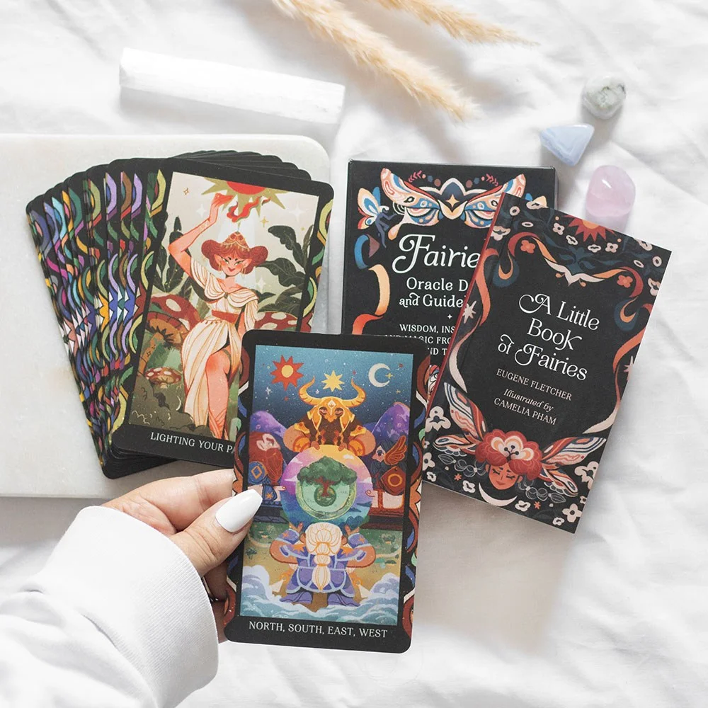 Fairies oracle card deck with colorful cards spread out beside an illustrated guidebook and magnetic closure box