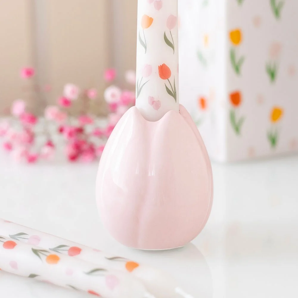 Ceramic tulip candle holder in soft pastel tones holding a white taper candle on a white background