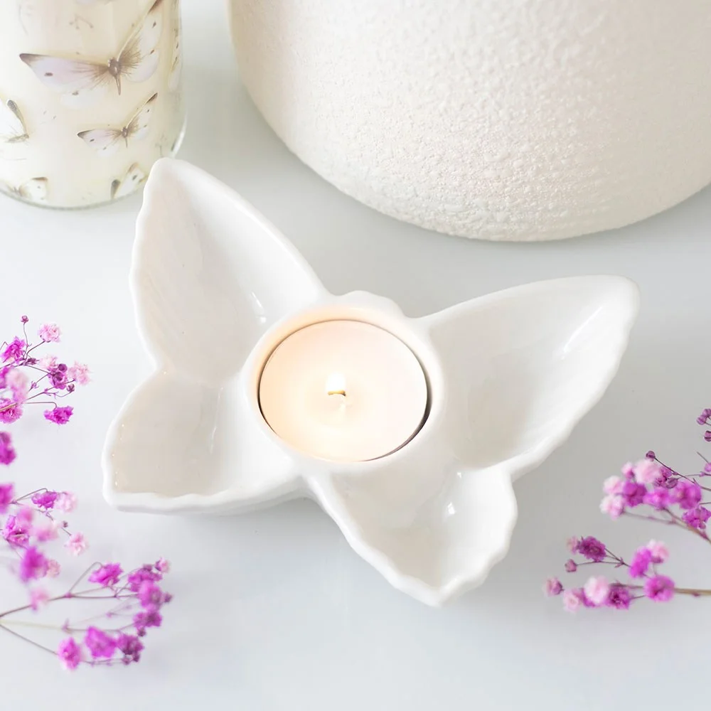 White ceramic butterfly tealight holder with a single lit candle in the centre on a white background