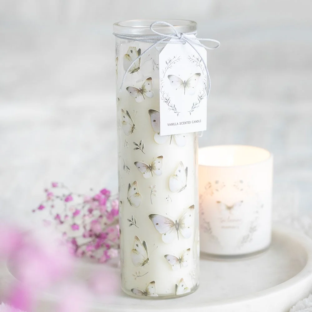 White butterfly print vanilla scented candle in a clear glass tube with lit wick and soft glowing flame