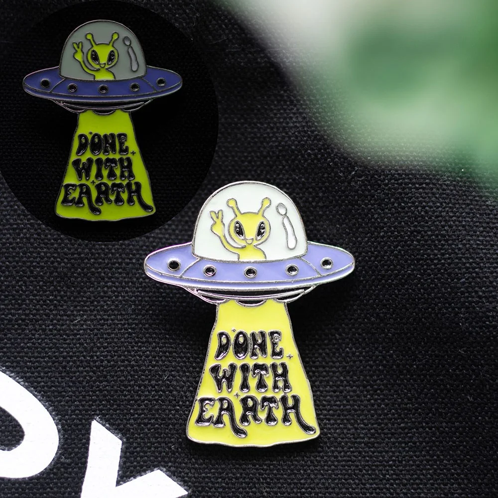 Glow in the dark pin featuring a UFO design with green and silver enamel details on a white background