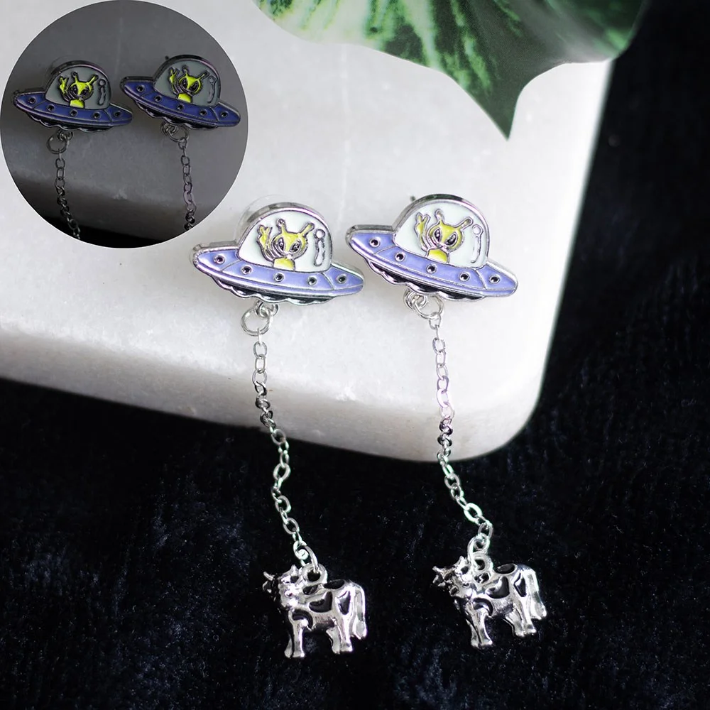 Glow in the dark earrings featuring dangle UFOs abducting cows with a silver-tone alloy finish