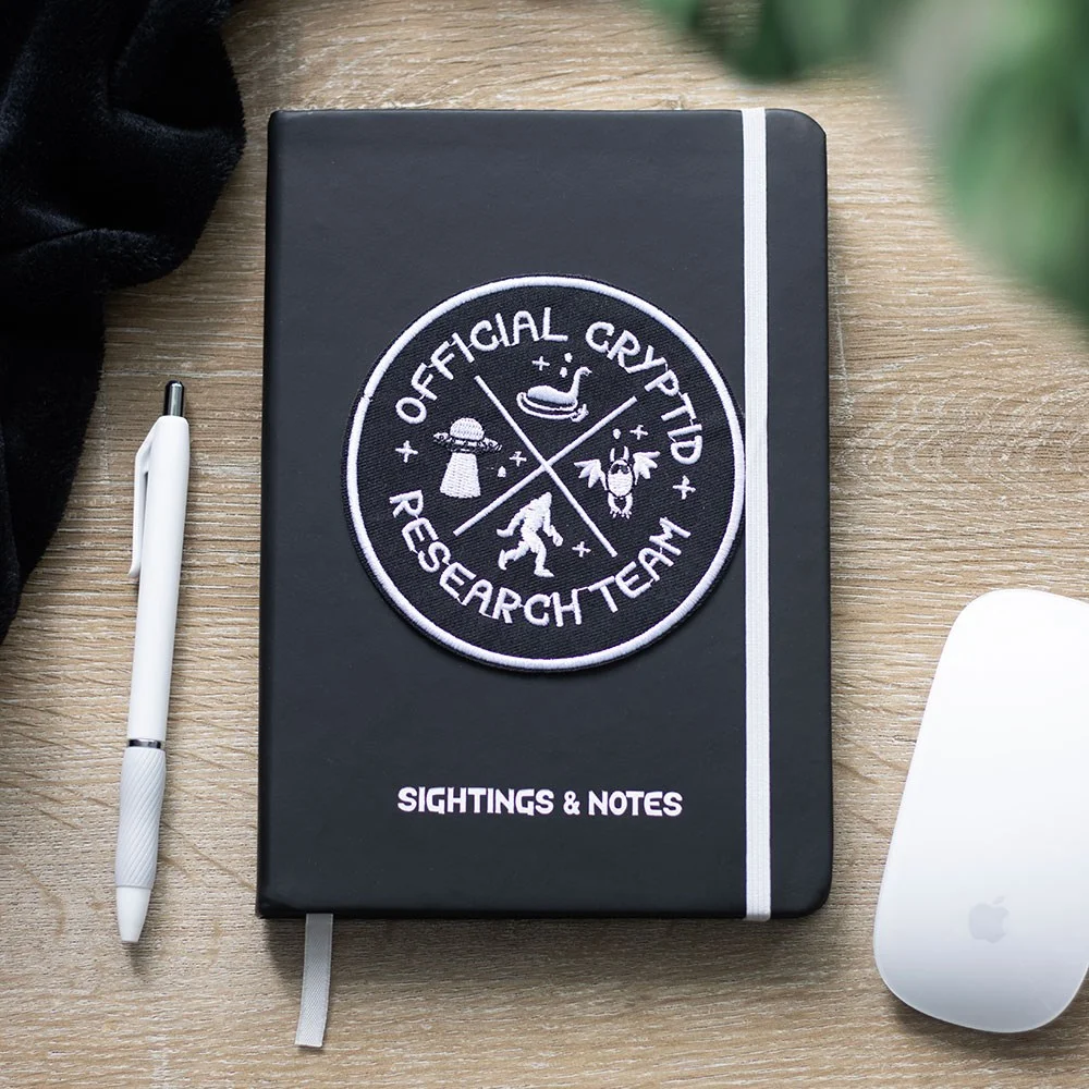 Cryptid Research Team A5 notebook with black cover and white text, open to lined pages for notes and sketches.